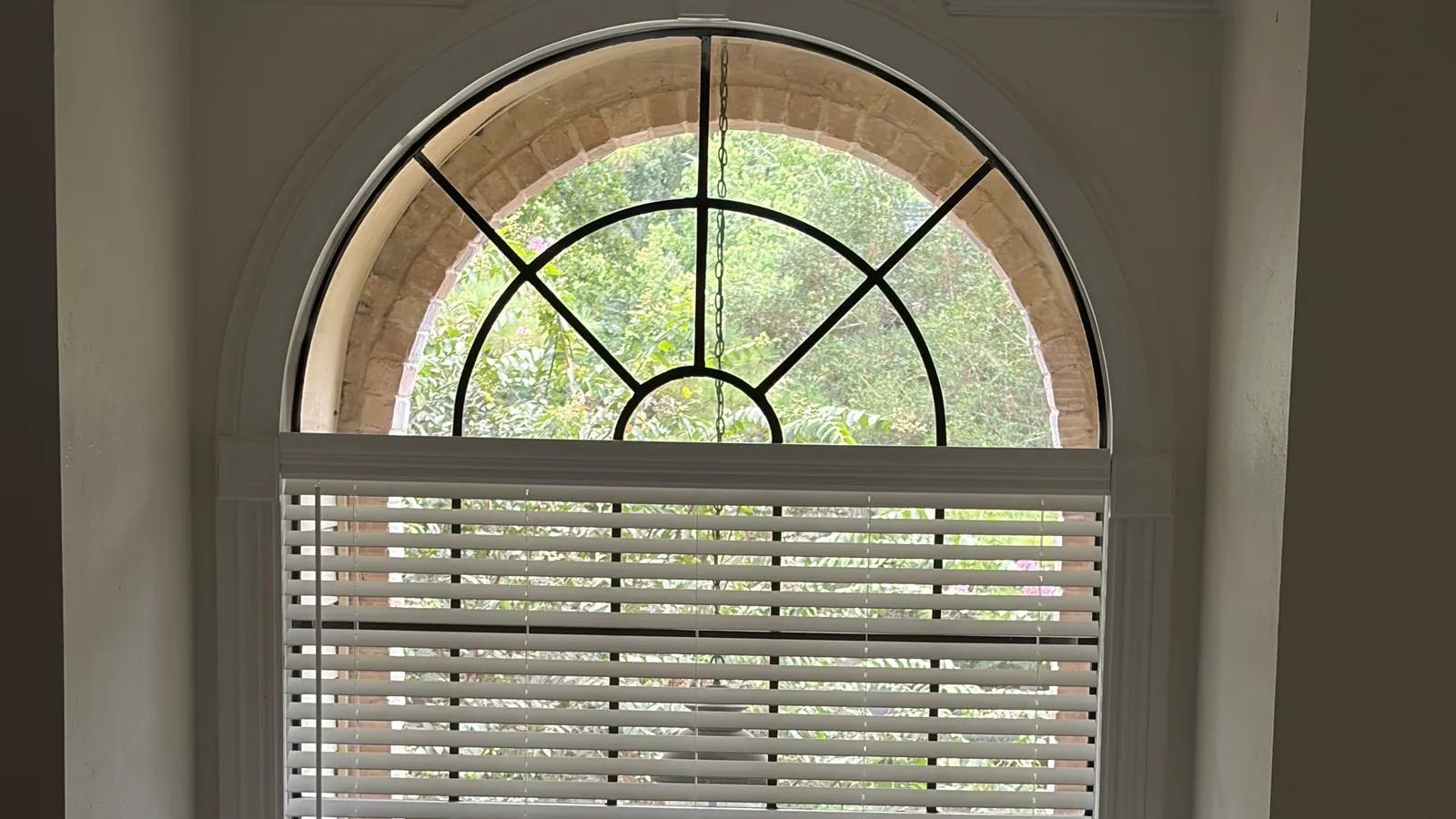 Two-inch faux wood blind covering the rectangular portion of a window while its decorative arch remains uncovered