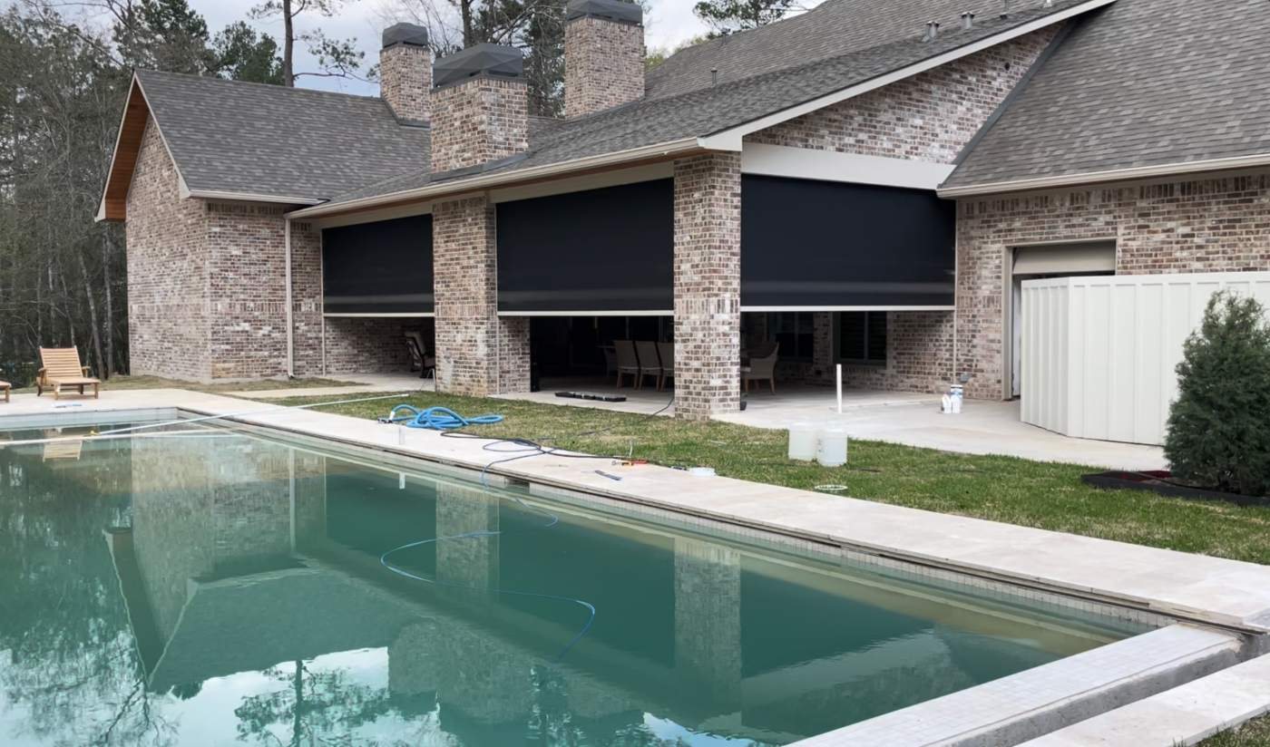 Motorized exterior roller shades lowered across a covered pool patio in Tomball, TX