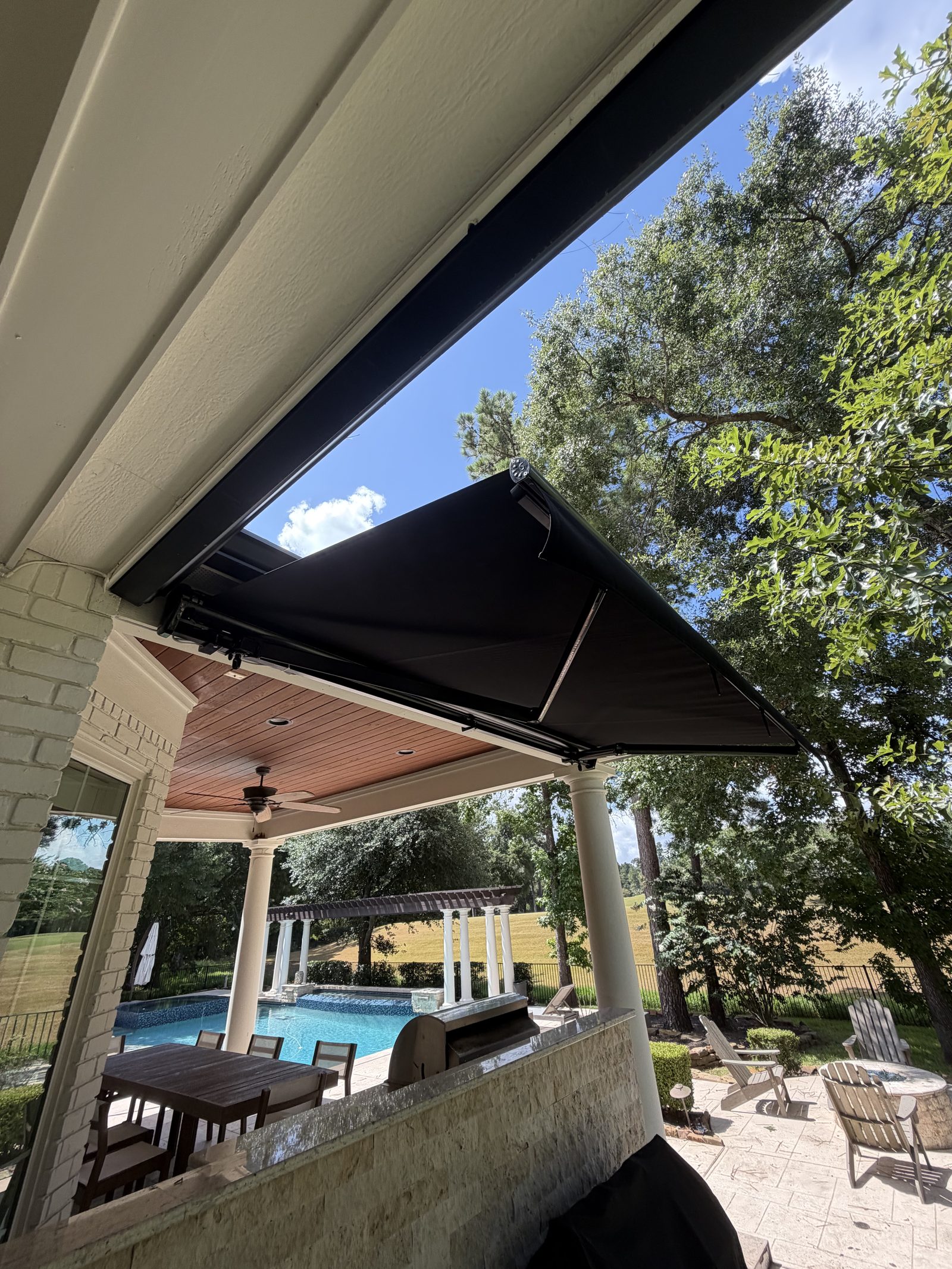 Motorized retractable awning in solid black, extended over a pool patio in The Woodlands, TX