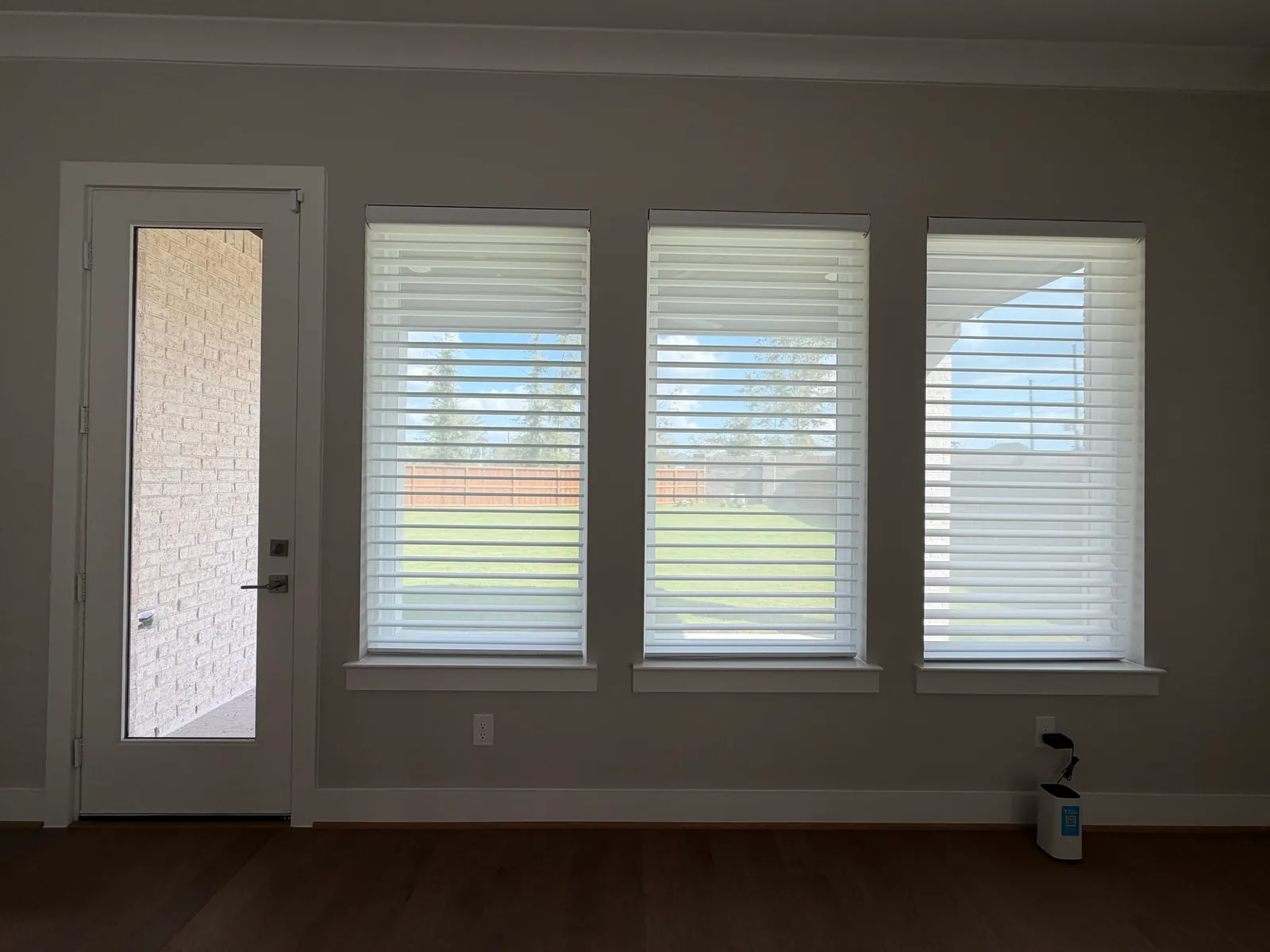 Three lowered white sheer shades with open vanes beside a glazed patio door.