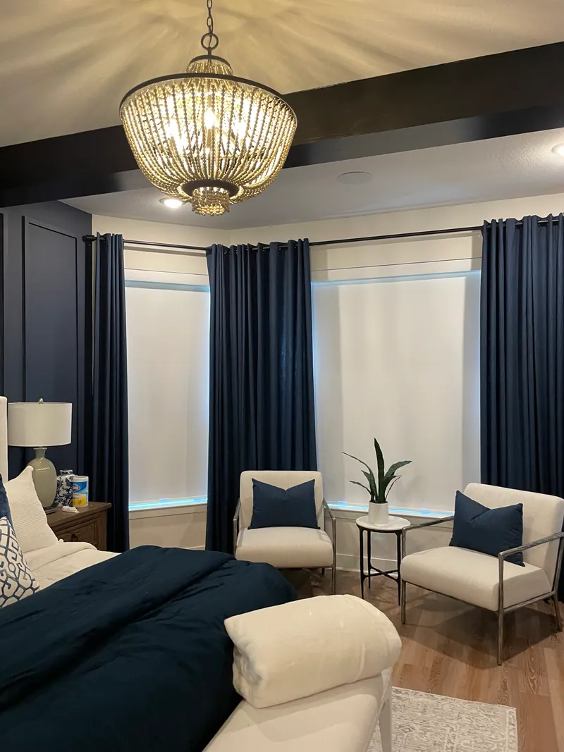 Blackout roller shade covering a main-bedroom window beside curtains.