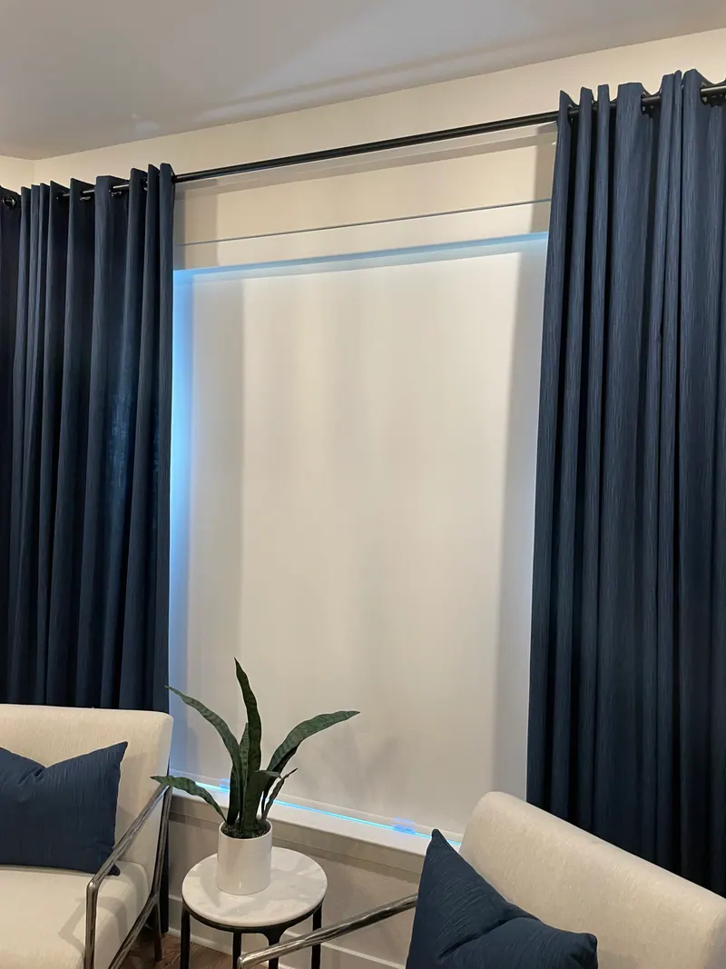 Blackout roller shade lowered behind bedroom curtains.