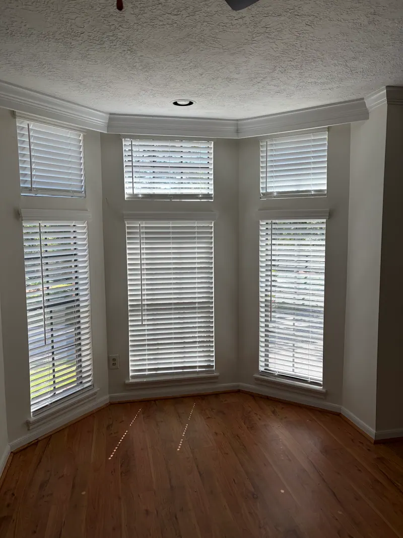 White faux wood blind beside a main-bedroom bed.