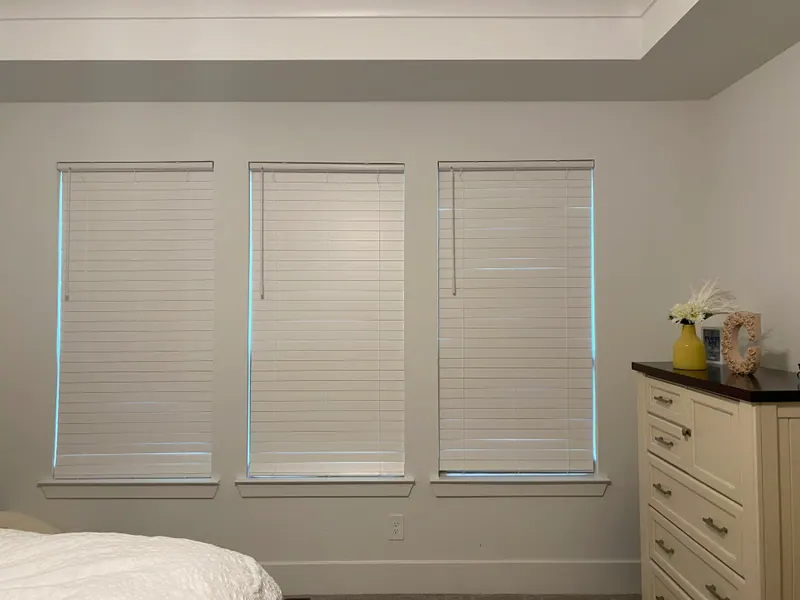 White faux wood blinds covering a bedroom window.