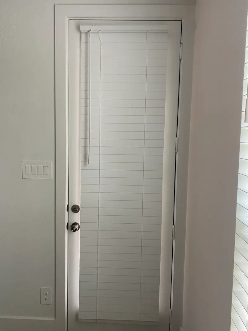 White faux wood blinds covering a glass patio door.