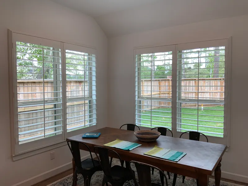 White plantation shutters covering two windows beside a breakfast table.
