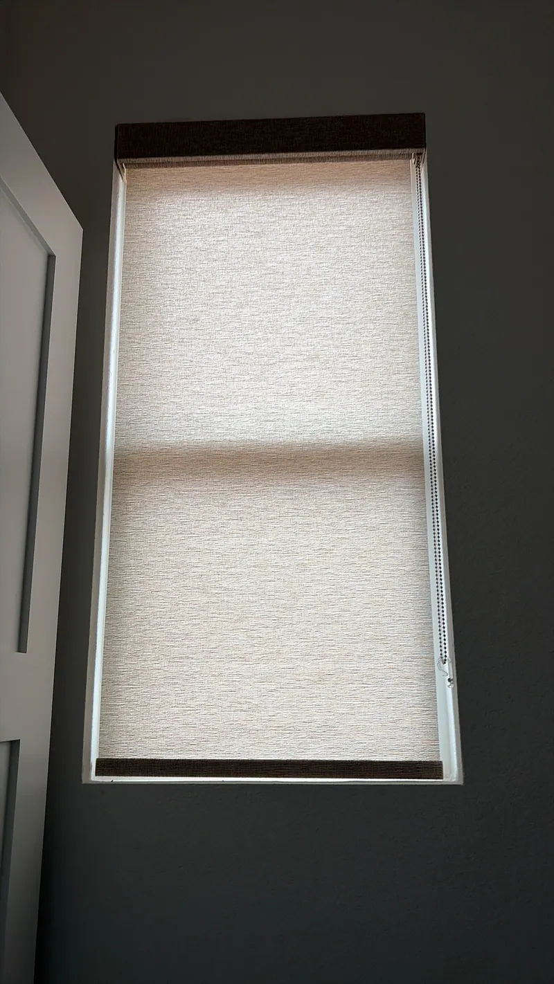 White roller shade lowered over a window beside a sofa.