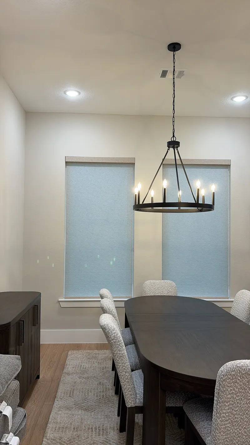 Light-colored roller shades covering tall windows in a sitting area.