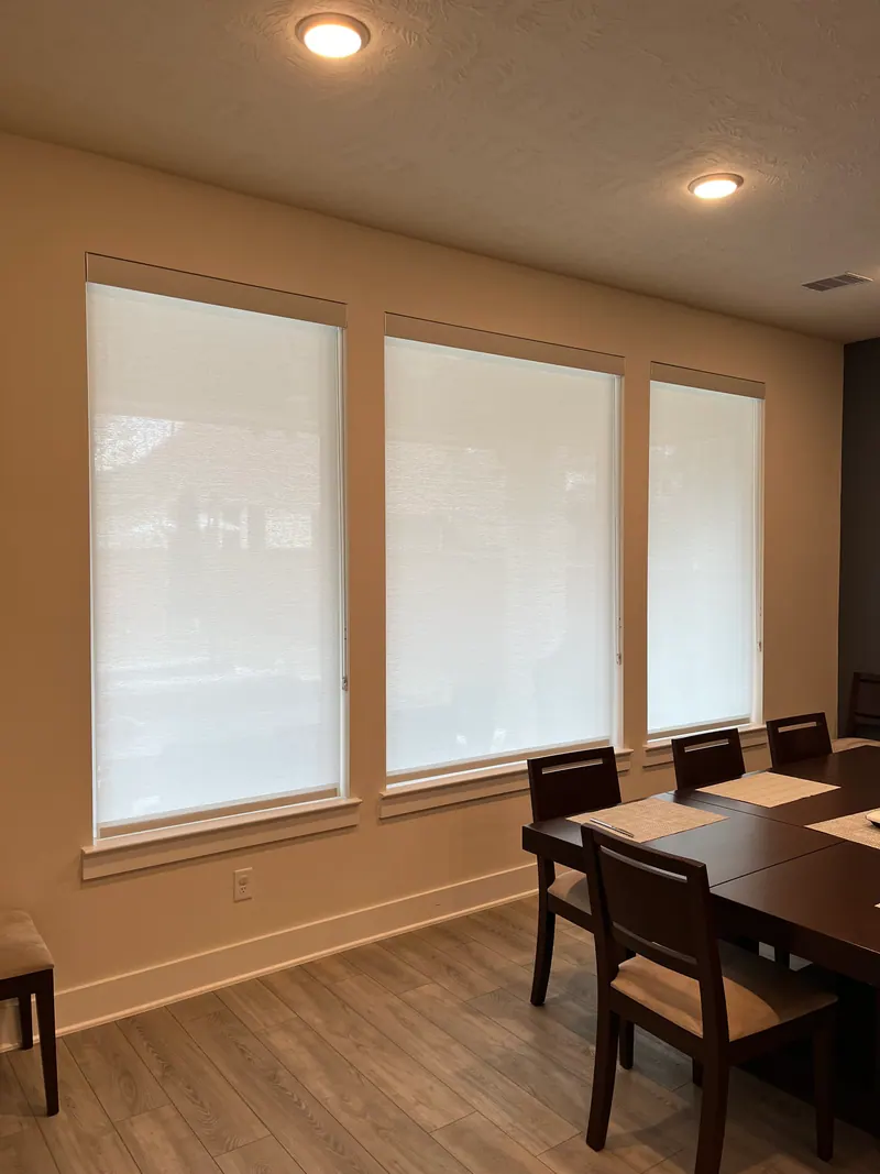 Light-filtering roller shades shown raised, partly lowered and closed over dining-room windows.